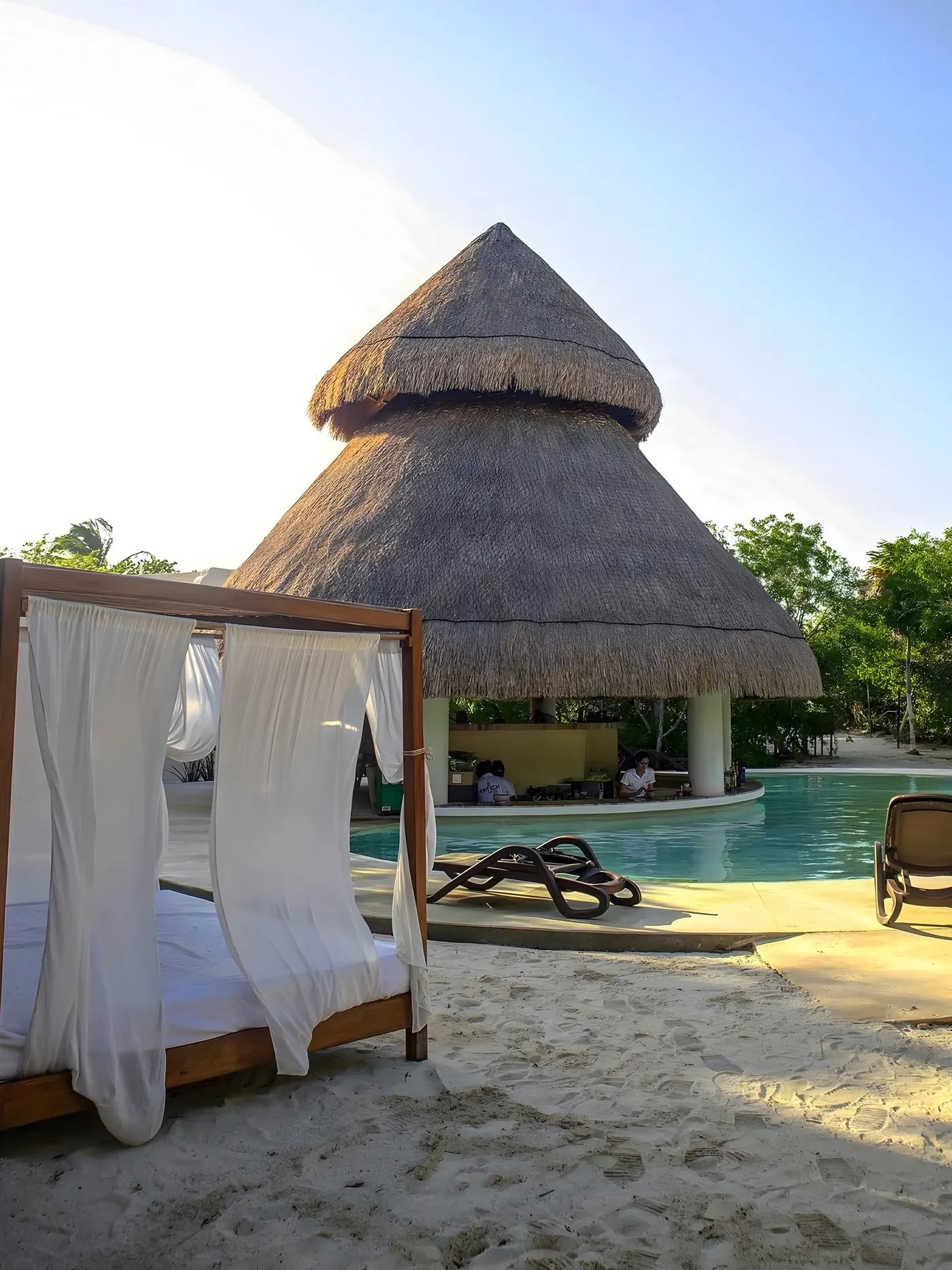 La palapa-bar al atardecer, con camastros y cama balinesa sobre la arena