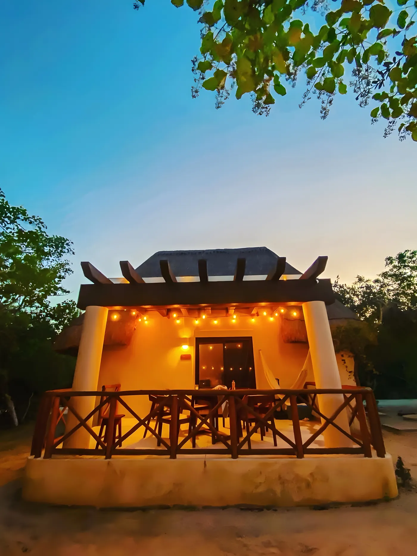 Bungalow al anochecer: terraza iluminada con comedor y hamaca