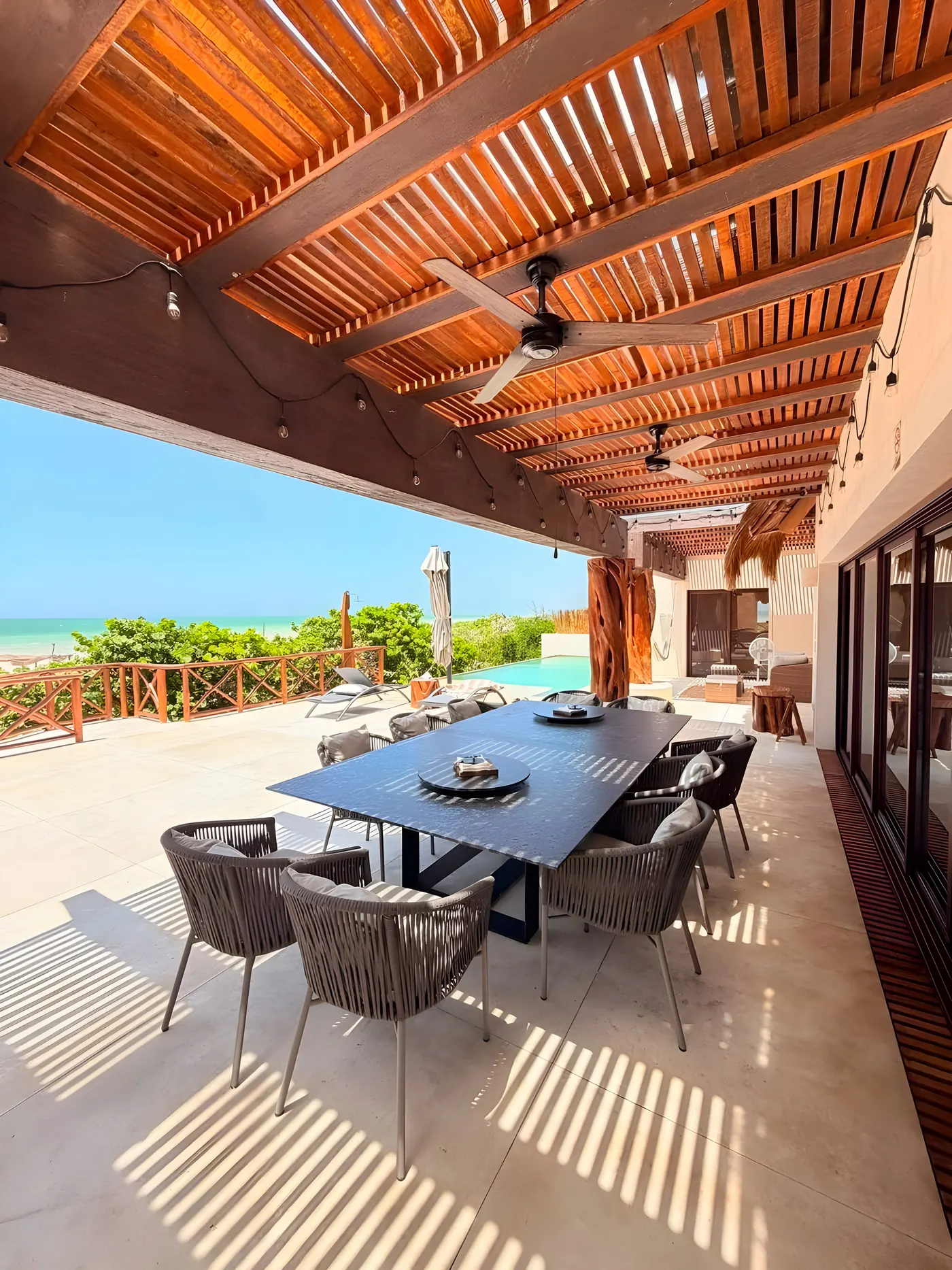 Comedor exterior de Casa María bajo la pérgola de madera, con el mar al fondo
